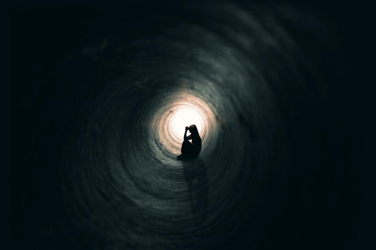 Die Silhouette einer betenden Frau, die in einem dunklen Tunnel mit einem Licht am Ende sitzt.