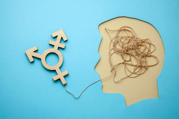 Transgender-Symbol an einem Faden befestigt, der in ein ausgeschnittenes Papierprofil eines Kopfes führt.