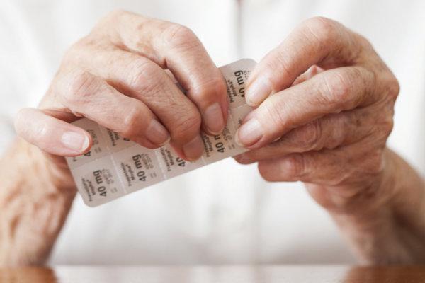 Hände einer alten Person halten ein Blister mit Statin-Tabletten.