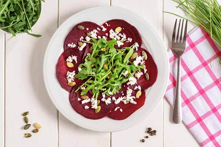 Beetroot carpaccio with rucola leaves and pumpkin seeds on wooden white background.