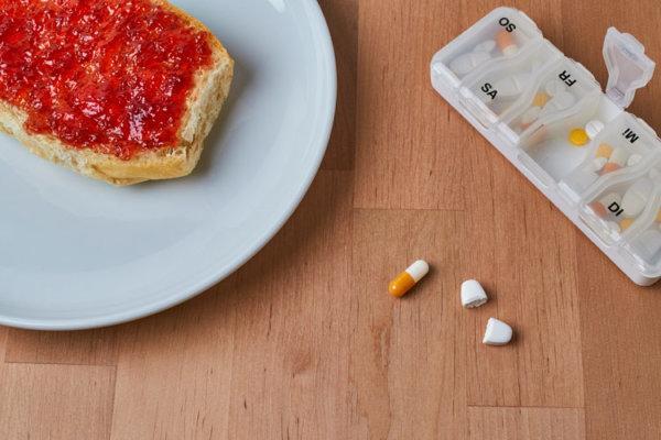 Marmeladen-Brötchen auf einem Teller und Tabletten auf einem Holztisch.