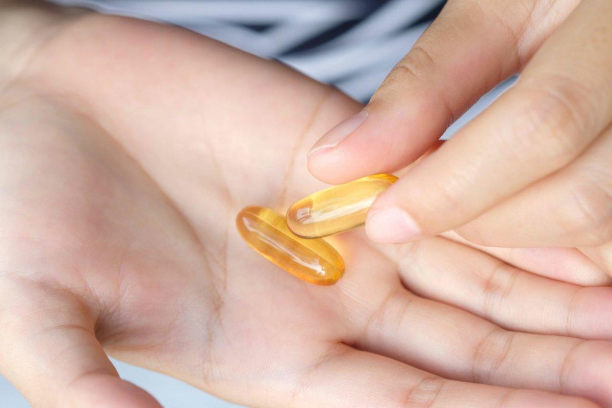 Fatty fish oil and vitamin E on the hand of a woman She will take health and wellness supplements and medical concepts.