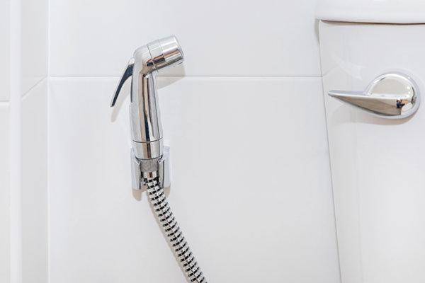 Griff einer Po-Dusche hängt neben einer Toilette.