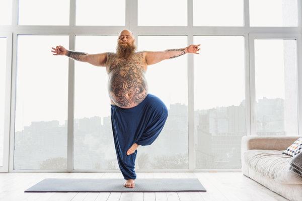Tätowierter Mann macht Yoga zuhause vor grosser Fentserfront