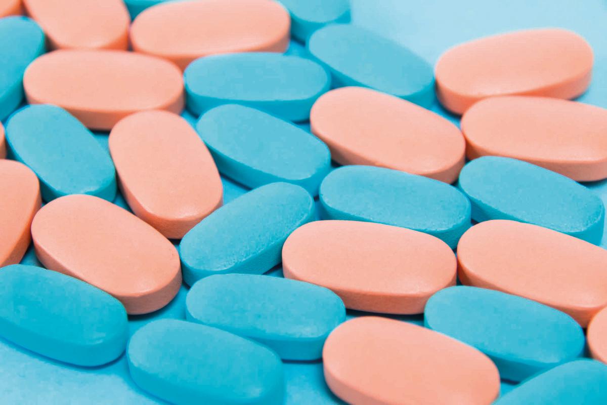 Modèle, vitamines bleues et roses en pilules pour hommes et femmes sur fond plat en papier bleu.