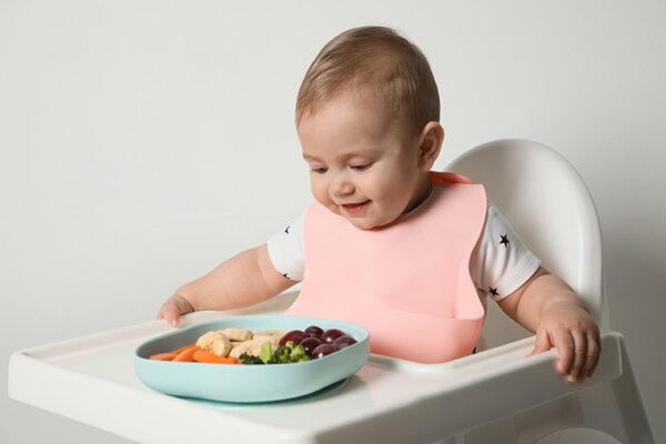 Niedliche kleine Baby trägt Lätzchen beim Essen auf weißem Hintergrund